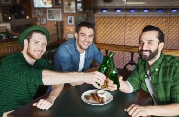 leisure, friendship and st patricks day celebration concept - happy male friends drinking beer and clinking bottles at bar or pub. friends drinking beer in bottles at bar or pub