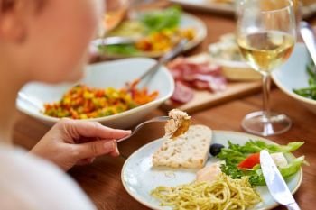 food and people concept - hands of woman with fork and knife eating pasta and chicken at wooden table. hands of woman eating pasta with chicken