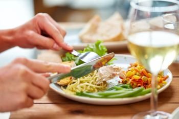 food and people concept - hands of woman with fork and knife eating pasta and chicken meat at wooden table. hands of woman eating pasta with chicken meat