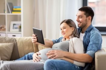 pregnancy, technology and people concept - happy man and his pregnant wife with tablet pc computer at home. man and pregnant woman with tablet pc at home