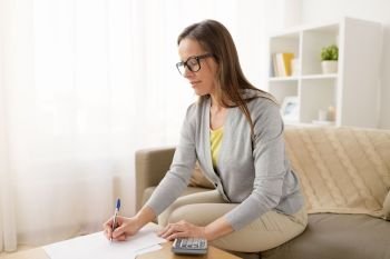 business, savings, finances and people concept - middle-aged woman with papers and calculator at home. woman with papers and calculator at home