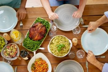 thanksgiving day, eating and leisure concept - group of people having roast chicken or turkey and pasta for dinner at table with food. group of people with chicken and pasta on table