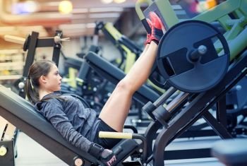 fitness, sport, bodybuilding, exercising and people concept - young woman flexing muscles on leg press machine in gym. woman flexing muscles on leg press machine in gym