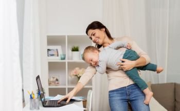 motherhood, multi-tasking, family and technology concept - happy mother with baby, laptop computer and papers working at home. happy mother with baby and laptop working at home