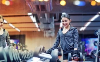 fitness, sport, exercising, weightlifting and people concept - smiling young woman choosing dumbbells in gym. smiling young woman choosing dumbbells in gym
