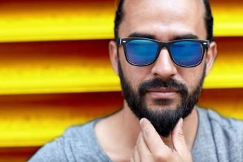fashion, style, eyewear and people concept - close up of man in sunglasses touching beard over ribbed yellow wall background. close up of man in sunglasses touching beard