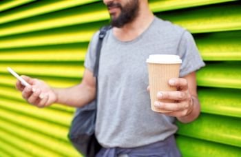 drinks, technology and people concept - close up of man with coffee cup and smartphone on street over ribbed yellow wall background. man with coffee cup and smartphone over wall