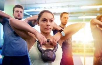 sport, fitness, weightlifting and training concept - group of people with kettlebells and heart-rate trackers exercising in gym. group of people with kettlebells exercising in gym