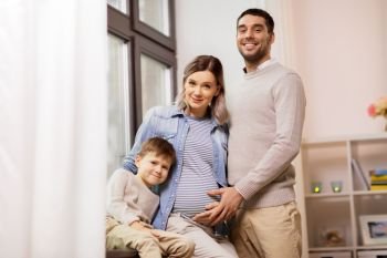 pregnancy, people and family concept - happy pregnant mother, father and little son hugging on sofa at home. happy family with pregnant mother at home