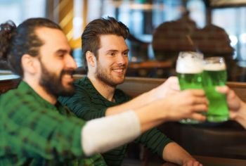 leisure, friendship, st patricks day and celebration concept - happy male friends drinking green beer and clinking glasses at bar or pub. male friends drinking green beer at bar or pub