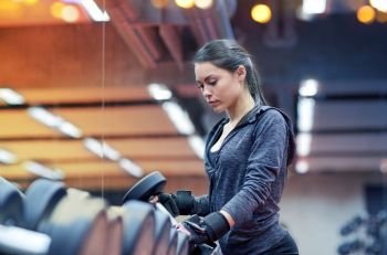fitness, sport, exercising, weightlifting and people concept - young woman choosing dumbbells in gym. young woman choosing dumbbells in gym