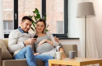 pregnancy, technology and people concept - happy man and his pregnant wife with smartphones at home. man and pregnant wife with smartphone at home