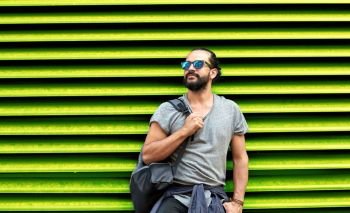 travel, tourism, lifestyle and people concept - man in sunglasses with bag standing at city street over ribbed green wall background. man in sunglasses with bag standing at street wall