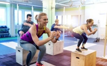 fitness, sport, training and exercising concept - group of people with heart-rate trackers doing box jumps in gym. group of people doing box jumps exercise in gym