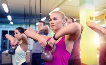 sport, fitness, weightlifting and training concept - group of people with kettlebells and heart-rate trackers exercising in gym. group of people with kettlebells exercising in gym