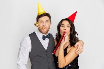 birthday, celebration and holidays concept - happy couple with party blowers and caps having fun. happy couple with party blowers having fun
