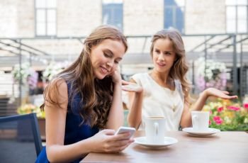 technology, internet addiction and people concept - young woman using smartphone and sad friend drinking coffee at cafe outdoors. young women with smartphone and coffee at cafe