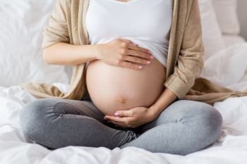 pregnancy, people and maternity concept - pregnant woman sitting in bed at home and touching bare belly. pregnant woman with bare belly sitting in bed