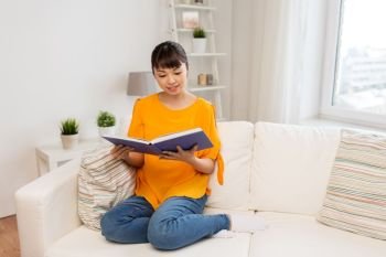 education, literature and people concept - smiling young asian woman reading book at home. smiling young asian woman reading book at home