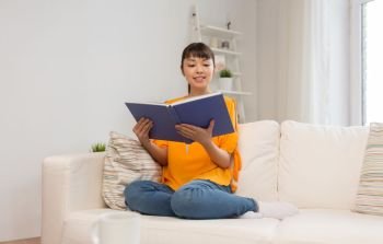 education, literature and people concept - smiling young asian woman reading book at home. smiling young asian woman reading book at home