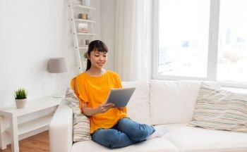 people, technology and leisure concept - happy young asian woman sitting on sofa with tablet pc computer at home. happy young asian woman with tablet pc at home