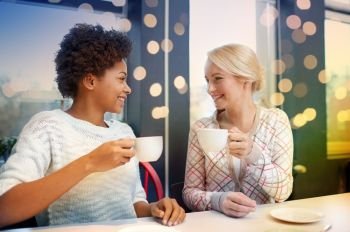 people, leisure, friendship and communication concept - happy young women meeting and drinking tea or coffee at cafe. happy young women drinking tea or coffee at cafe