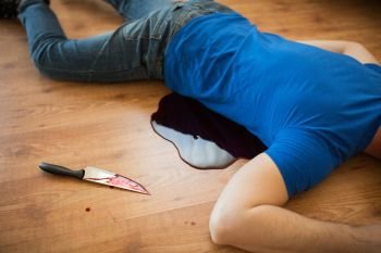 murder, kill and people concept - dead man body and knife in blood lying on floor at crime scene (staged photo). dead man body lying on floor at crime scene