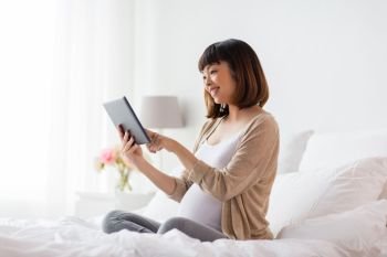 pregnancy, technology, people and expectation concept - happy pregnant asian woman with tablet pc computer in bed at home. happy pregnant asian woman with tablet pc at home