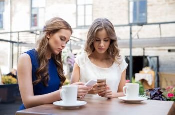 technology, lifestyle, internet addiction and people concept - young women with smartphones drinking coffee at cafe outdoors. young women with smartphones and coffee at cafe