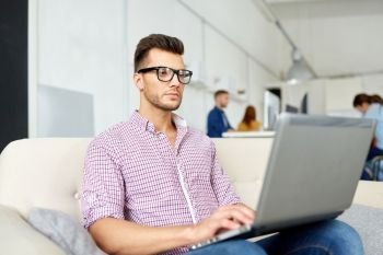 business, education, technology and people concept - young man in eyeglasses with laptop computer working at office. man in eyeglasses with laptop working at office