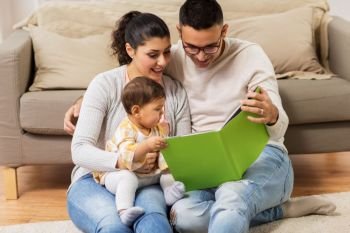 family, parenthood and people concept - happy mother, father and baby daugter reading book at home. happy family with baby reading book at home