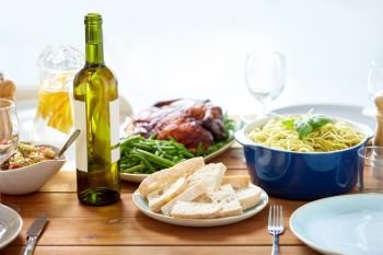 food, thanksgiving day and eating concept - bottle of wine with bread, pasta and roast chicken on served wooden table. bottle of wine and food on served wooden table