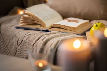 hygge and cozy home and literature concept - book with autumn leaf and blanket on sofa. book with autumn leaf and blanket on sofa at home