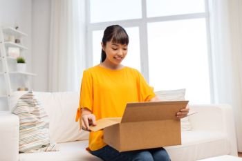 people, delivery and shipping concept - happy asian young woman with parcel box at home. happy asian young woman with parcel box at home