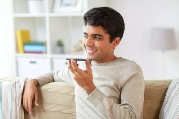 technology, communication and people concept - happy smiling man using voice command recorder on smartphone at home. man using voice command recorder on smartphone