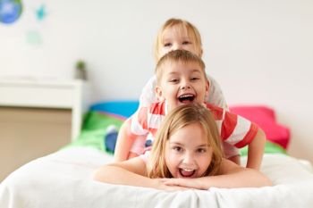 childhood, leisure and family concept - happy little kids having fun in bed at home. happy little kids having fun in bed at home