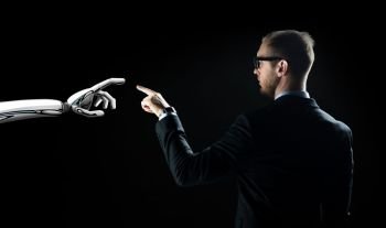 business, future technology and artificial intelligence concept - businessman and robot hand over black background. robot and human hand flash light over black