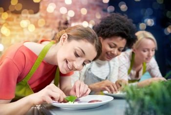 cooking class, friendship, food and people concept - happy women cooking and decorating plates with dishes in kitchen. happy women cooking and decorating dishes