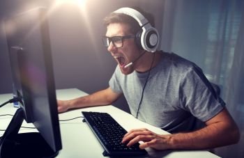 technology, gaming, entertainment, let’s play and people concept - angry screaming young man in headset with pc computer playing game at home and streaming playthrough or walkthrough video. man in headset playing computer video game at home