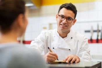 people, fast food and cooking concept - happy smiling chef at restaurant writing order and customer. chef at fast food restaurant writing order