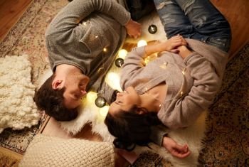 leisure, hygge and people concept - happy couple with garland lying on floor at home. happy couple with garland lying on floor at home