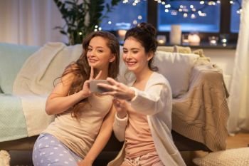 friendship, hygge and technology concept - happy female friends or teenage girls taking selfie by smartphone at home. female friends taking selfie by smartphone at home