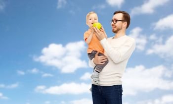 family, healthy eating and people concept - happy father and and little son with green apple over blue sky and clouds background. happy father and little son with green apple