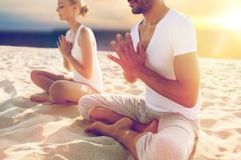 yoga , mindfulness, harmony and people concept - close up of couple meditating on beach. close up of couple meditating on beach