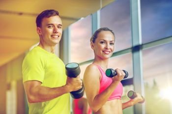 sport, fitness, lifestyle and people concept - smiling man and woman with dumbbells exercising in gym. smiling man and woman with dumbbells in gym