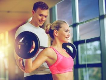 sport, fitness, lifestyle and people concept - smiling man and woman with barbell exercising in gym. smiling man and woman with barbell in gym