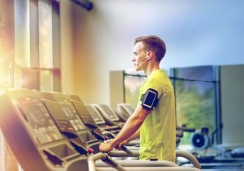 sport, fitness, lifestyle, technology and people concept - man with smartphone and earphones exercising on treadmill in gym. man with smartphone exercising on treadmill in gym