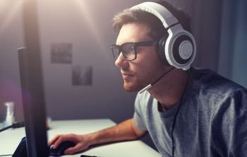 technology, gaming, entertainment, let’s play and people concept - young man in headset and glasses with pc computer playing game at home and streaming playthrough or walkthrough video. man in headset playing computer video game at home