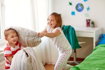 childhood, leisure and people concept - happy kids playing and fighting by pillows at home. kids playing and fighting by pillows at home