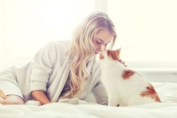 pets, morning, comfort, rest and people concept - happy young woman with cat in bed at home. happy young woman with cat in bed at home